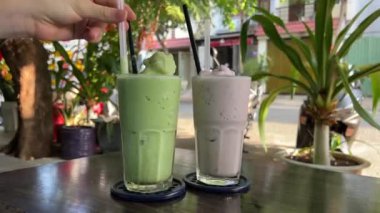 İki milkshake yaban mersini ve avokado nanesi sokak kafesinde tropik bir ülkede pipetle karıştırılır. Yüksek kalite 4k görüntü