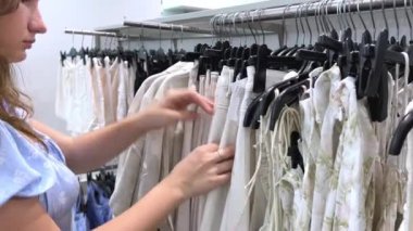 Giyim mağazasında genç bir kız hafif yazlık elbiseler seçiyor. Kadın giyim mağazası Kadın günlük kıyafet alışverişi yapıyor moda kadın giyim mağazası, butik teftişi farklı