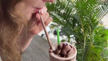 Pembe manikürlü bir kadın eli, açık mermer bir masadan büyük bir bardak çikolatalı kahve smoothie alır. Yakın plan. Nefis, lezzetli bir içecek kız çikolatalı milkshake içiyor.