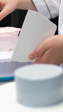 Kadın pastacı mutfak masasının üzerine eğildi ve bej kremayı bir hamur torbasından bej bento kekinin yarısına sıkıştırdı. Sabit karıştırıcı yakında duruyor. 
