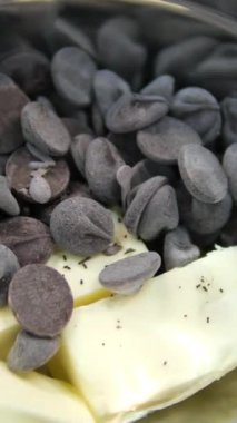 Kakao yağı parçaları bir tabak siyah çikolatanın üzerine serpiştirilir. Şekerleme ürünlerinin hazırlanması. Koyu çikolata ve tereyağı tabakta