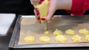 Pasta poşeti yardımıyla küçük ekler yapmak. Eklentiler için hamur borularını yavaş çekimde pişirme kağıdına döküyorum. Eklentiler için Choux hamur işi 