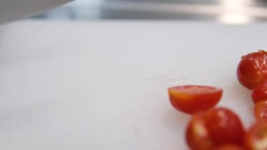 Kadın elleri bıçakla salata ya da yemek için vişneli domates kesiyor. Daldaki domatesleri delip geçti. Şef kiraz domateslerini takozlara klipsliyor. Yavaş çekim. 