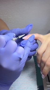 Erkek parmaklarının tırnak etlerini tırnak matkabıyla yavaş çekimde kesiyoruz. Yakın plan tanınmayan profesyonel güzellik uzmanı genç Kafkasyalı için manikür yapıyor.
