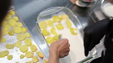 Kadın cam bir tabakta patates katmanına tavuk eti koyar. Evde yemek pişirmek. tavuklu patates graten.