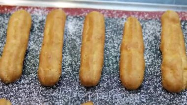 Freshly Baked Eclairs Lined Up in Display at a Pastry Shop. Close-up view of fresh, golden eclairs filled with creamy custard, showcased in a pastry shop. Perfect for dessert enthusiasts. 