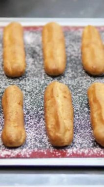 Freshly Baked Eclairs Lined Up in Display at a Pastry Shop. Close-up view of fresh, golden eclairs filled with creamy custard, showcased in a pastry shop. Perfect for dessert enthusiasts. 
