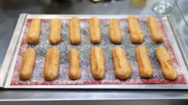 Freshly Baked Eclairs Lined Up in Display at a Pastry Shop. Close-up view of fresh, golden eclairs filled with creamy custard, showcased in a pastry shop. Perfect for dessert enthusiasts. 