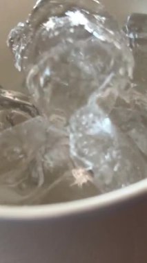 Köpüklü su bardağı düşen buz küpü. Ağır çekimde buz soğuk maden suyuna düşer. Beyaz arka planda köpüklü soda. Cam su. Buzlu yaz içkisi. Köpüklü içecek. bar içeceği.