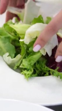 Kadın eli, vişneli domatesleri salatayla birlikte bir tabağa koyar. Salatayı tabağa koy.