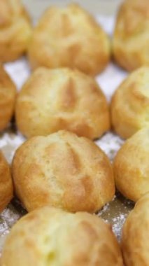 Choux ya da profiterol pişirirken, kadın elleri hamuru torbadan fırın kağıdına sıkıştırır, genel görünüm. Çikolatalı craquelin ile kremalı ve çilekli choux pişiriyorum. Vanilyalı choux. Yüksek kalite 