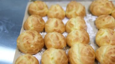 Choux ya da profiterol pişirirken, kadın elleri hamuru torbadan fırın kağıdına sıkıştırır, genel görünüm. Çikolatalı craquelin ile kremalı ve çilekli choux pişiriyorum. Vanilyalı choux. Yüksek kalite 
