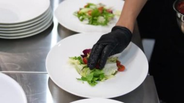 Kadın eli, vişneli domatesleri salatayla birlikte bir tabağa koyar. Salatayı tabağa koy.