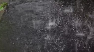 Yaz mevsiminde ağır yağmur damlalarının asfalt üzerindeki su birikintilerine düşüşü yavaş çekimde gerçekleşiyor. Şiddetli yağmur, yağmur mevsimi. yağmur birikintisi