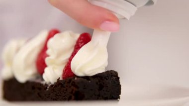 Çikolatalı Brownie, çilekli ve kremalı. Çilekleri kremayla süsleyin. Çileklerin üzerine krema döken çikolatalı brownie tatlısından leziz yemekler.