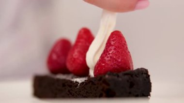 Aşçı Pavlova tatlısı pişiriyor, pastaları kremayla süslüyor. Yemeği kapat. Çikolatalı Brownie, çilekli ve kremalı. Çilekleri kremayla süsleyin.