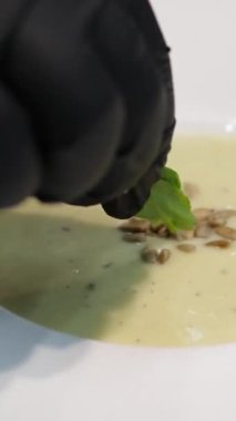 Krema çorbasını ayçiçeği tohumlarıyla servis etmek ve bir parça roka bir restoranda beyaz tabakta servis etmek mutfakta bir aşçı hazırlamak ve dekore etmek. Yüksek kalite 4k görüntü