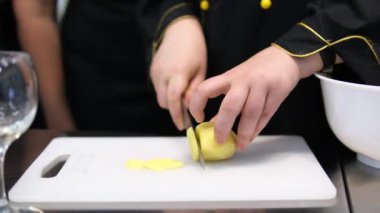 Erkek aşçı sebze yemeği pişirmek için çiğ patates keser, tahta kesmek için patates keser, hostes mutfağında yemek hazırlar, vejetaryen biri için lezzetli bir yemektir.