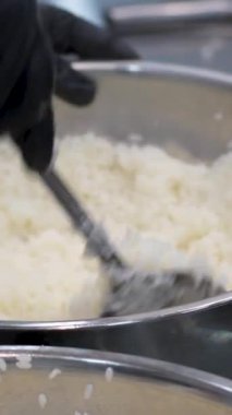 Profesyonel bir suşi şefinin elleri Norveç yapraklarının üzerine pirinç seriyor beyaz mutfak masasının üzerinde bambu bir hasırın üzerine uzanmış bir sıra taze sebze, biber ve marul yapraklarıyla birlikte..