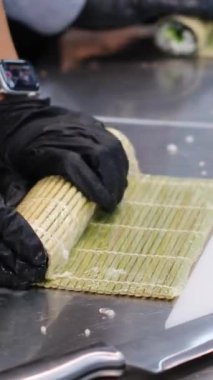 Profesyonel bir suşi şefinin elleri Norveç yapraklarının üzerine pirinç seriyor beyaz mutfak masasının üzerinde bambu bir hasırın üzerine uzanmış bir sıra taze sebze, biber ve marul yapraklarıyla birlikte..