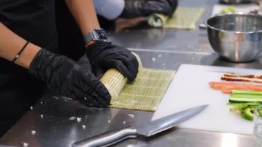 Profesyonel bir suşi şefinin elleri Norveç yapraklarının üzerine pirinç seriyor beyaz mutfak masasının üzerinde bambu bir hasırın üzerine uzanmış bir sıra taze sebze, biber ve marul yapraklarıyla birlikte..