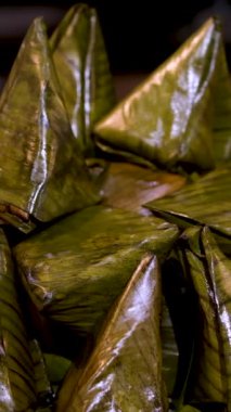 Tayland Tatlısı, buharda pilav, muz ve ahşap arka planda Nipa palmiye yapraklarına sarılmış siyah fasulye. Ana malzemeler Yapışkan Pirinç, Muz, Kara Fasulye ve Hindistan cevizi Sütü..