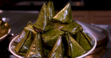 Tayland Tatlısı, buharda pilav, muz ve ahşap arka planda Nipa palmiye yapraklarına sarılmış siyah fasulye. Ana malzemeler Yapışkan Pirinç, Muz, Kara Fasulye ve Hindistan cevizi Sütü..