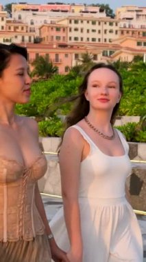 İki kız arkadaş köprüde el ele tutuşup fotoğraf çekiyorlar. Asya Avrupalı farklı milletler genç kadınların güzellik bakımı