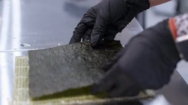Kepli ve peynirli suşi, aşama aşama pişmiş rulo suşi. Yakından yemek pişirir. Bir şef suşi yapar ve pirinç, kırmızı balık, avokado ve Philadelphia peynirinden rulo yapar.. 