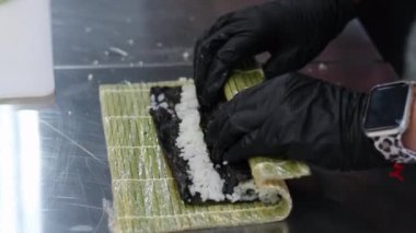 Kepli ve peynirli suşi, aşama aşama pişmiş rulo suşi. Yakından yemek pişirir. Bir şef suşi yapar ve pirinç, kırmızı balık, avokado ve Philadelphia peynirinden rulo yapar.. 