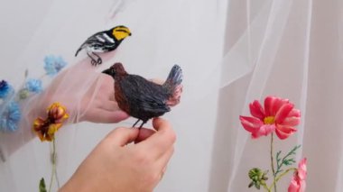 Çiçek nakışları ve duvağa takılmış kuşlar ince bir kumaş üzerinde bir kadın, parlak süslemeli bir manken gelinliğine el işi düzleştiriyor. Yüksek kalite 4k
