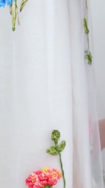 Çiçek nakışları ve duvağa takılmış kuşlar ince bir kumaş üzerinde bir kadın, parlak süslemeli bir manken gelinliğine el işi düzleştiriyor. Yüksek kalite 4k