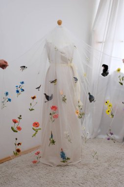 Çiçek nakışları ve duvağa takılmış kuşlar ince bir kumaş üzerinde bir kadın, parlak süslemeli bir manken gelinliğine el işi düzleştiriyor. Yüksek kalite 4k