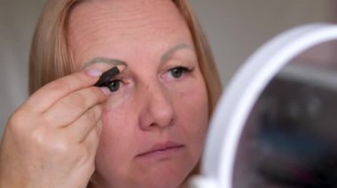 Kadın, dış hatları arasında kaş üzerine boya sürüyor. Aynaya bakıyor. Evde güzellik prosedürü yapan bir fırça kullanıyor. Modern moda stil, düzeltme, kaşların renkleri.