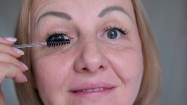 Yakın çekim, stilist kadın gözünün kirpiklerine siyah rimel sürüyor. Siyah rimel kullanan bir kadın. Profesyonel makyaj. Mua yapıyorum. Ağır çekim. Makyaj hocası sınıfı..