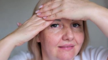 Alnındaki kırışıklıkları düzelt. Kaşlarını çatan kadın alnına dokunuyor. Yüzündeki kırışıklıkları elleriyle düzeltiyor. Alnındaki kaşlar arası kırışıklık. Cilt bakımı. Güzellik konsepti