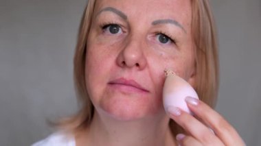 Odaklanmış kadın kusurları örtmek için yumuşak cilde sürtünür. Kızıl saçlı bayan bulanık arkaplanda akşam makyajına hazırlanıyor. leke temeli