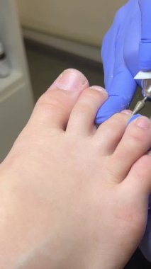 Usta ojeyle oje sürerek oje sürüyor, kurutuyor, kendine özen gösteren mavi lateks eldivenler, genç bayan bacak, yakın plan güzellik salonu pedikür uzmanı tırnak makasıyla tırnak kesiyor. pedikür salonu.