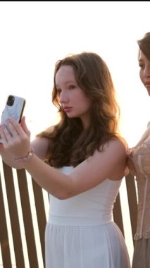 Arkadaşlar fotoğraf çekiyor. İki genç Asyalı kadın cep telefonu kullanarak selfie çekiyor. Çekici Avrupalı ve Asyalı bir kadın. Tatil aktivitesi, ya da modern yaşam tarzı konsepti. Yüksek kalite 