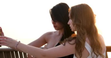 Arkadaşlar fotoğraf çekiyor. İki genç Asyalı kadın cep telefonu kullanarak selfie çekiyor. Çekici Avrupalı ve Asyalı bir kadın. Tatil aktivitesi, ya da modern yaşam tarzı konsepti. Yüksek kalite 