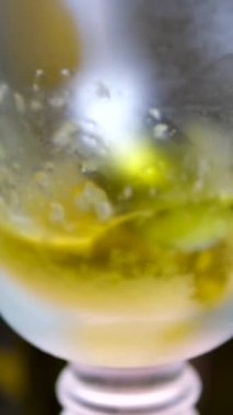 Gri arka planda, yaşlanmayı önleyen kozmetik malzemeleri formüle eden soyut kozmetik malzemeleri üzerine boş bir zeytinyağı şişesine dökülüyor. donmuş zeytinyağı taneleri