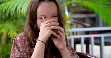 Palmiye ağaçlarının yanındaki terasta Vietnamlı kahvesi içen genç bir kız tropikal bir ülkede, pahalı bir otelde bir kafede oturmuş içkinin tadını çıkarıyor. Yüksek kalite 