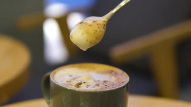 Üst cam manzaralı, arka planda köpüklü latte ve çikolatalı kurabiye. El kaşıklarının yakın çekim videosu lezzetli karıştırılmış latte köpüğü ile çay kaşığı konsept kahve sipariş etmek ve rahatlamak için kafeyi ziyaret edin.