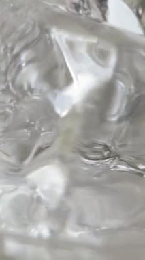 Yakın çekim buz küpleri yavaş çekimde dönüyor. Su dalgaları soğuk içeceklerle çevrili hareket eden büyük donmuş blokları kapladı. Makro kokteyl sıvısı üst görünüm. Serin yaz içeceği konseptini tazeliyorum. 4k 