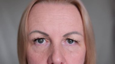 Yukardan, yorgun kahverengi gözlü, siyah maskaralı, üzgün, olgun bir kadının yakın çekimi. Makyajlı, cildinde kırışıklıklar olan son sınıf model bir kadın. Kırpılmış atış.