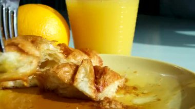 Akçaağaç şuruplu kruvasan, portakal suyu ve portakal suyunun arka planında bıçak ve çatalla taze pişmiş kruvasan kesiyor. Pencereden güneş ışığı