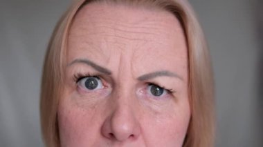 Yukardan, yorgun kahverengi gözlü, siyah maskaralı, üzgün, olgun bir kadının yakın çekimi. Makyajlı, cildinde kırışıklıklar olan son sınıf model bir kadın. Kırpılmış atış.