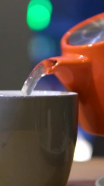 Ev hanımı çaydanlıktan, içinde çay poşeti olan şeffaf fincana sıcak su döker. Kadın, mutfakta öğle yemeği molası için aromatik amfibik çay demler. Yüksek kalite 4k görüntü