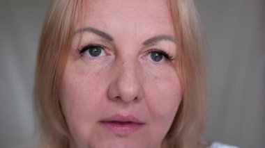 Üzgün kadın, üzgün yaşlı, yorgun, kahverengi gözlü, siyah maskaralı yaşlı kadının yakın çekimini üstten yapar. Makyajlı bir kadın, cildinde kırışıklıklar var. Kesilmiş atış. 4k