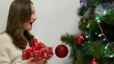 Gülümseyen, meraklı genç bir kadın, erkek ya da kocanın parlak mavi deniz mavisi kutusunda kırmızı saten kurdeleyi açıyor. Sarışın kadın süslenmiş şöminenin önünde Noel hediyesiyle oturuyor..
